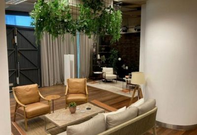 Lounge area with tan leather armchairs, a grey sofa, and hanging greenery over a wooden coffee table.