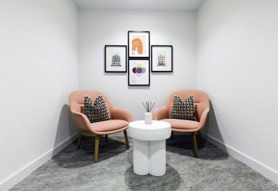 Cosy breakout nook with two coral-colored armchairs and decorative framed prints.