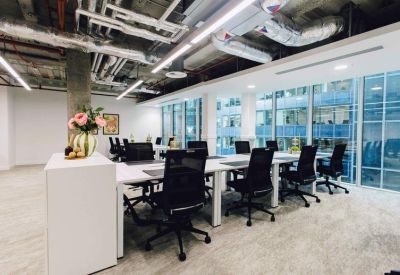 Bright open-plan workspace with white desks, ergonomic black chairs, and large windows.