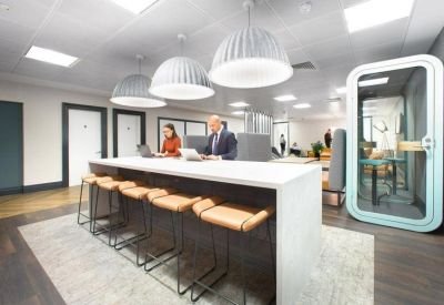 Modern coworking space with a long white communal table, leather bar stools, and large pendant lights.