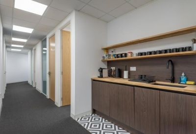 Kitchenette area in a hallway with dark wood cabinets and a coffee station.
