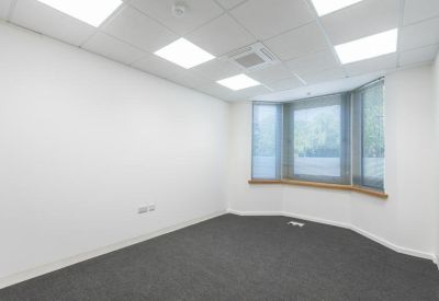 Bright private office with large bay window and grey carpeting.