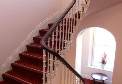 Grand curved staircase with dark red carpeting and white ornate spindles.