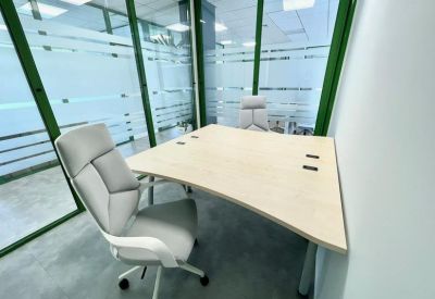 Glass-enclosed private office with a white corner desk and ergonomic chair.