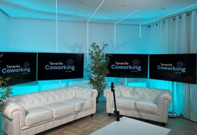 Bright communal lounge with white tufted sofas, blue neon lighting, and several wall-mounted screens.
