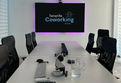 Meeting room with a long table, ergonomic chairs, and a large screen displaying a logo.