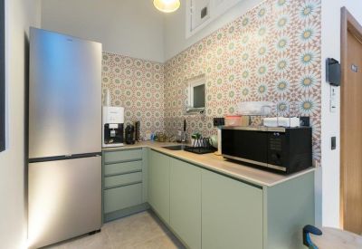 Modern communal kitchen area with green cabinets, patterned backsplash tiles, and stainless steel fridge.