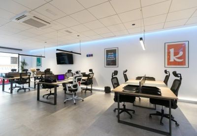 Bright open-plan office workspace with wooden desks, ergonomic black chairs, and blue accent lighting.