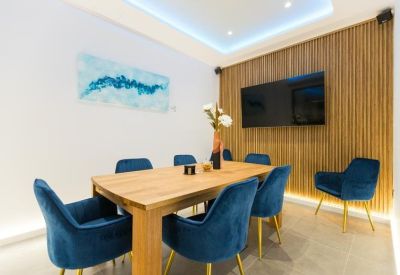 Meeting room with a wooden table, blue velvet chairs, and a slatted wood feature wall with a large TV.