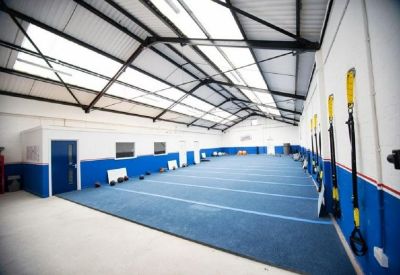 Large indoor fitness or training area with blue flooring and suspension training equipment.