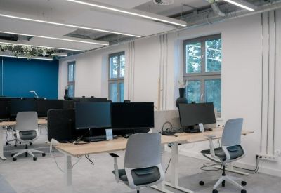 Bright workspace featuring several ergonomic desks and large windows.