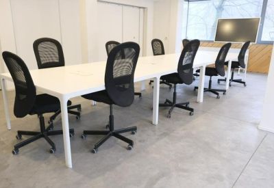 Co-working space with long white desks and ergonomic mesh chairs.