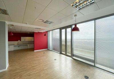 Empty office suite with light wood floors, red accent walls, and large floor-to-ceiling windows.