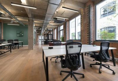 Bright office workspace with rows of white desks and black mesh chairs.