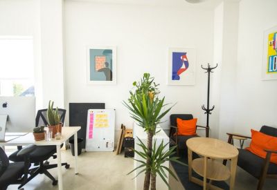 Bright breakout area with white walls, framed illustrations, and orange accent cushions.