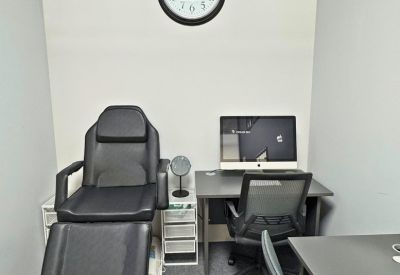 Private office space featuring a black treatment chair, desk with computer, and a wall clock.