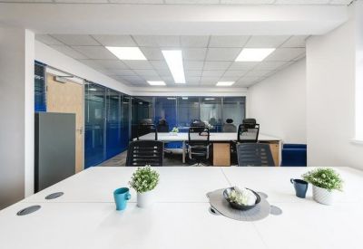 Modern coworking space with a central white table and glass-walled meeting rooms.