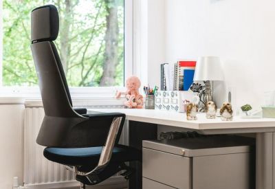 Private office desk with an ergonomic chair and natural light from a large window.