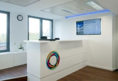 Bright reception area featuring a white desk with a colorful logo and digital information screen.