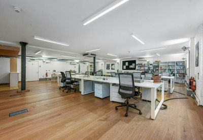 Modern open-plan workspace with white desks and warm wood flooring.