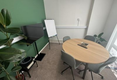 Modern meeting room with a round wooden table, grey chairs, and a wall-mounted TV.