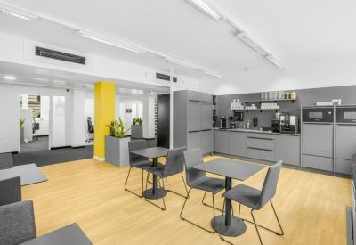 Modern communal kitchen and dining area with grey cabinetry and light wood flooring.