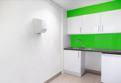 Clean communal kitchen area with vibrant lime green backsplash and white cabinetry.