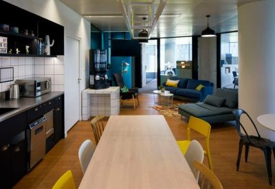 Modern office kitchen and breakout area with a long wooden table and blue sofas.