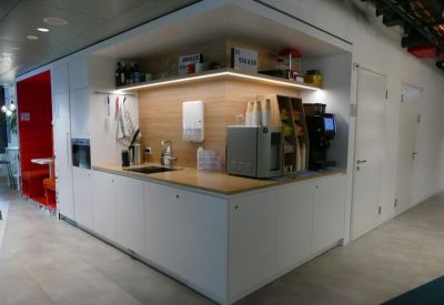 Clean, white kitchen breakout area with coffee machines and a wood-paneled backsplash.