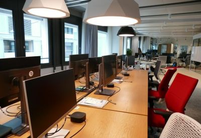 Long wooden desk with multiple monitors and vibrant red office chairs.
