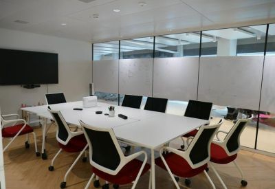 Professional meeting room with a large screen and white table with red-accented chairs.