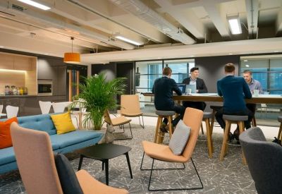 Lounge area with colorful sofas, armchairs, and professionals working at a long communal table.