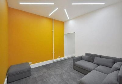 Bright breakout space with an orange feature wall and grey corner sofa.