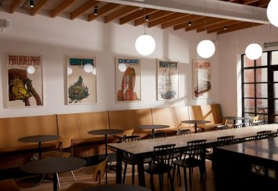 Communal dining area with long tables, booth seating and vintage travel posters.