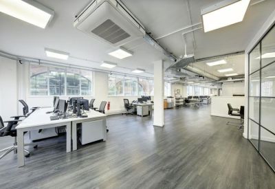Bright open-plan office with white desks, ergonomic chairs, and dark wood-style flooring.