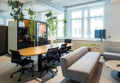 Casual breakout area with a long wooden table, lounge seating, and hanging plants.