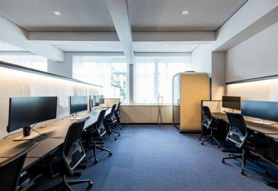 Bright workspace featuring several desks with large monitors and ergonomic chairs.