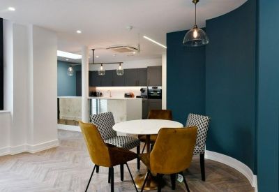 Communal dining area with yellow velvet chairs and a deep teal feature wall.