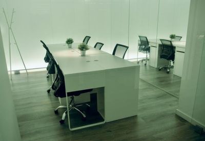 Spacious white coworking area featuring long desks and black mesh office chairs.