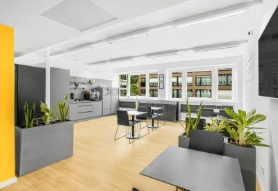 Communal kitchen and dining area with wooden floors, indoor plants, and cafe-style seating.