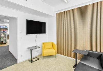 Breakout corner with a yellow armchair, leather sofa, and a wall-mounted TV.
