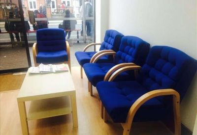 Waiting area with a coffee table and four blue upholstered chairs near a glass entrance.