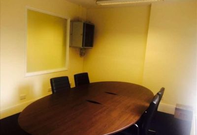 Small meeting room with an oval wooden table and three black leather chairs.