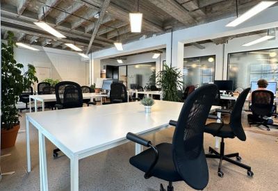 Bright open-plan office with white desks and black mesh chairs under an industrial ceiling.
