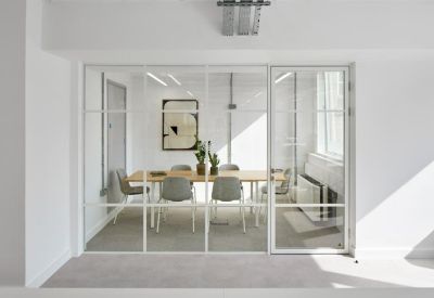 Glass-walled meeting room with a wooden table and grey chairs.