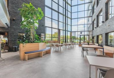 Atrium communal space with tall glass walls, indoor trees, and dining tables.