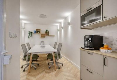 Bright dining and break area with a long white table, grey chairs, and a modern coffee station.