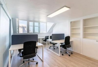 Modern open-plan office with white desks, black chairs, and natural light from large windows.