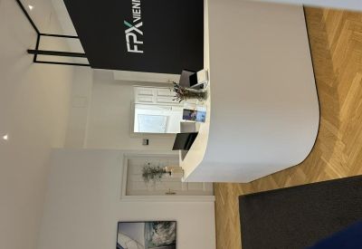 Modern white curved reception desk with a black branded backdrop and light wood flooring.