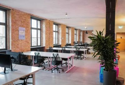 Open office layout with exposed brick walls, white desks, and large potted plants.